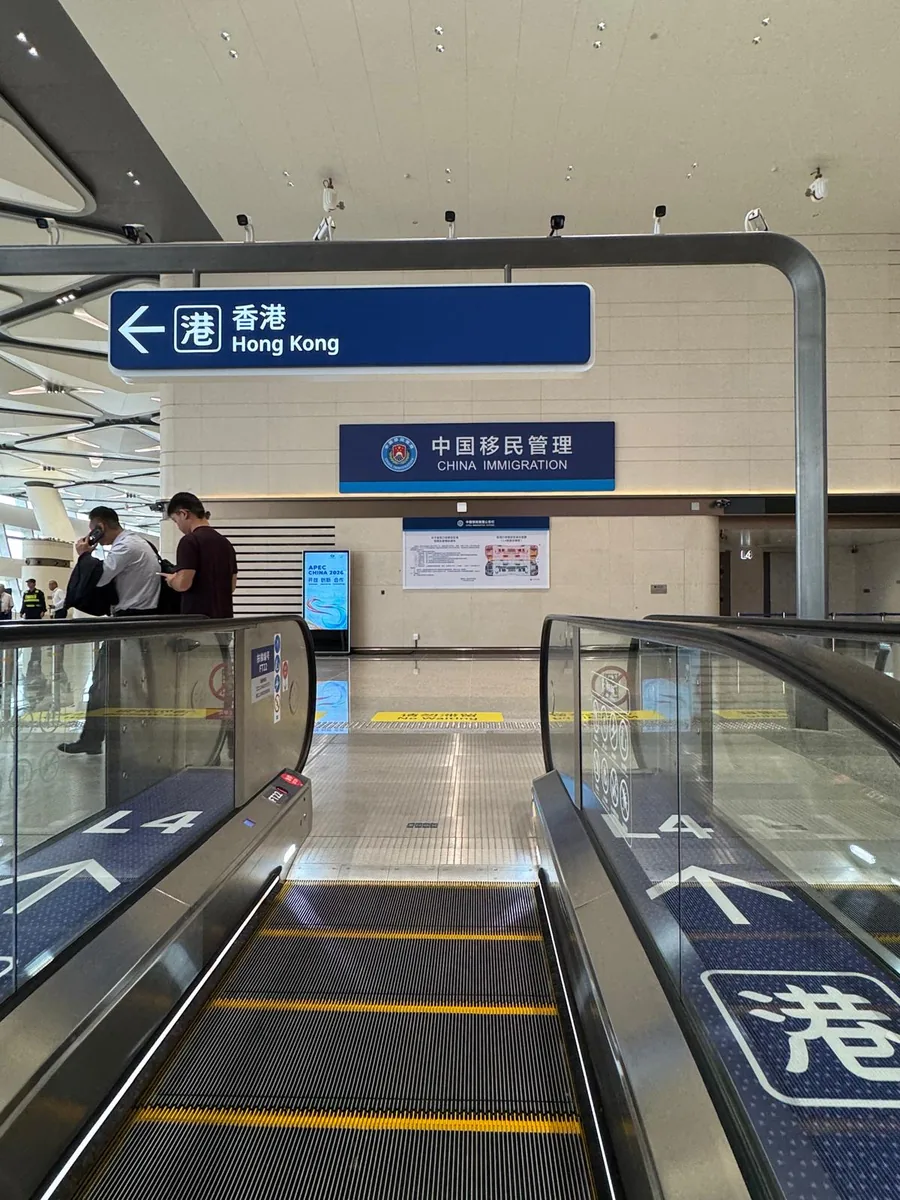 中国側出境エリア（CHINA IMMIGRATION）へ向かうエスカレーターと「香港 Hong Kong」の青い案内看板